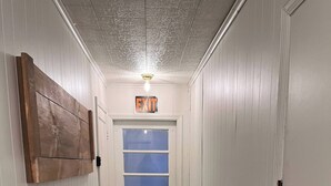 Ein Flur mit einer weißen Tür, einem Fenster mit blauem Rahmen und einem an der Wand befestigten Holzgegenstand.
