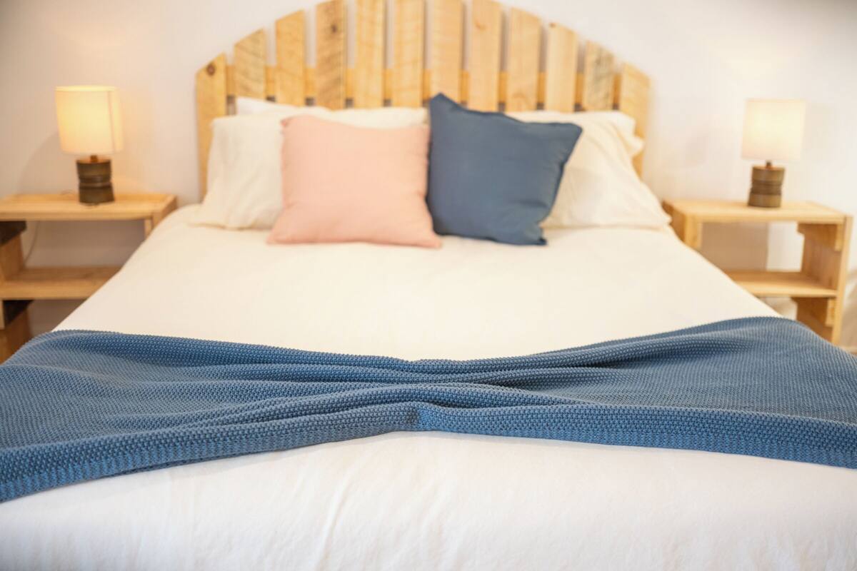 A bed with a wooden headboard, two bedside lamps, and a blue blanket.