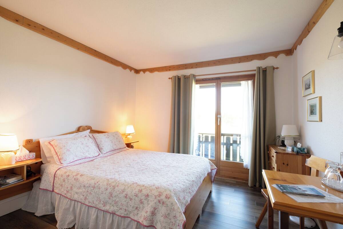A bedroom with a bed, bedside tables, a wooden desk, and a balcony door.