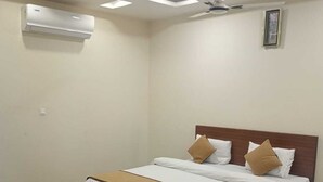 A bedroom with a bed, bedside tables, an air conditioning unit, and a ceiling fan. - HOTEL SHIVALIKA (Jaipur)