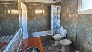 Une salle de bain avec un meuble-lavabo en bois, une baignoire, des toilettes et un bidet.