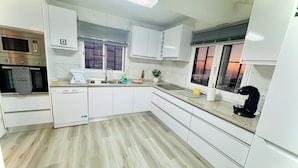 Een moderne keuken met witte kasten, een ingebouwde oven, een magnetron en een koffieapparaat.