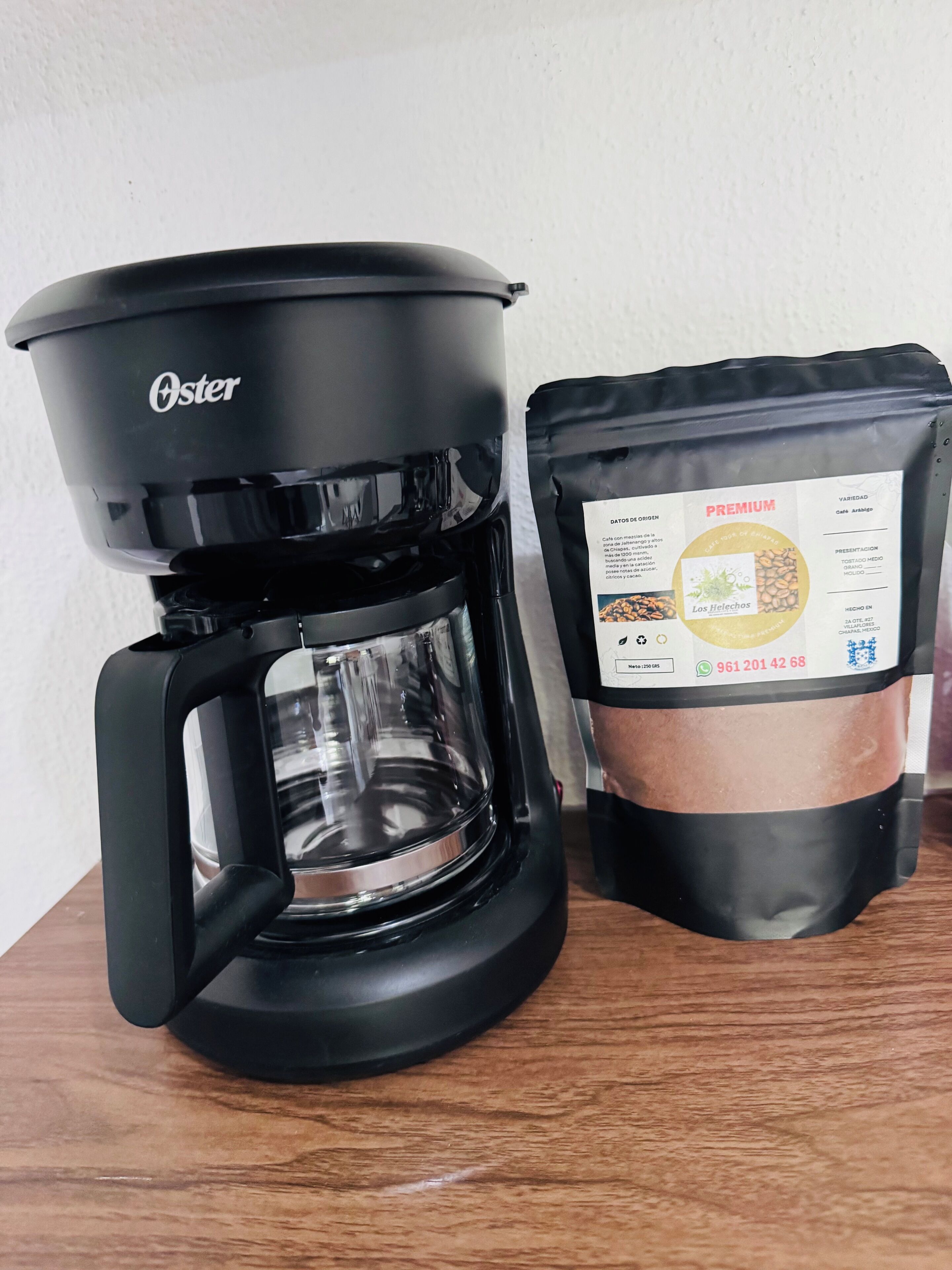 A black Oster coffee maker and a bag of coffee on a wooden table.