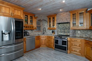 A kitchen with wooden cabinets, a stainless steel refrigerator, a stove, and a dishwasher. - 'Amongst the Clouds,' a one-of-a-kind retreat. (Blowing Rock)