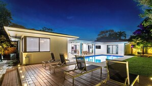 Ett modernt hus med en swimmingpool, solstolar och en täckt uteplats.