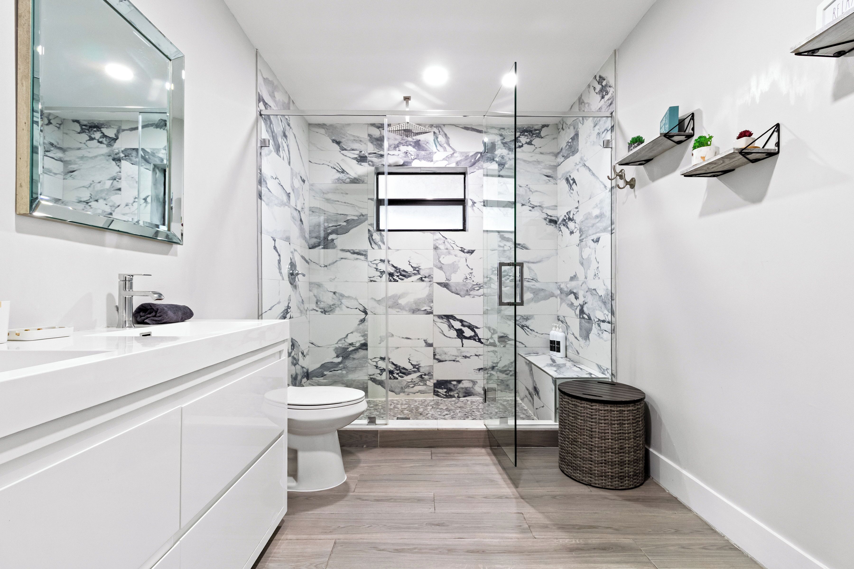 A modern bathroom with a marble wall, a glass shower enclosure, a white sink, and a toilet.