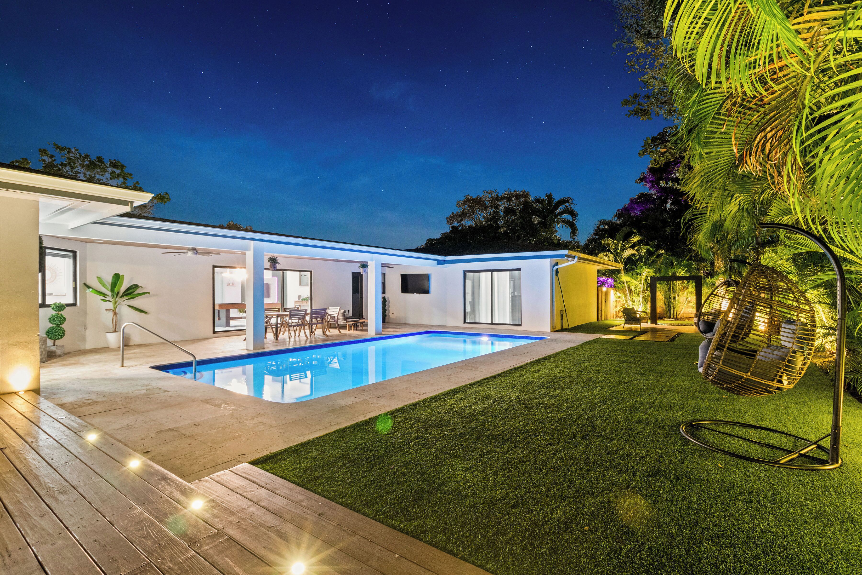 A modern house with a swimming pool, a patio, and a hanging chair.