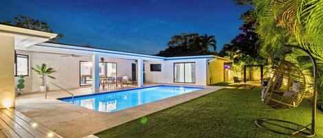 A modern house with a swimming pool, a patio, and a hanging chair.