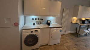 A compact kitchen with a washing machine, a microwave, and a small countertop with various appliances.