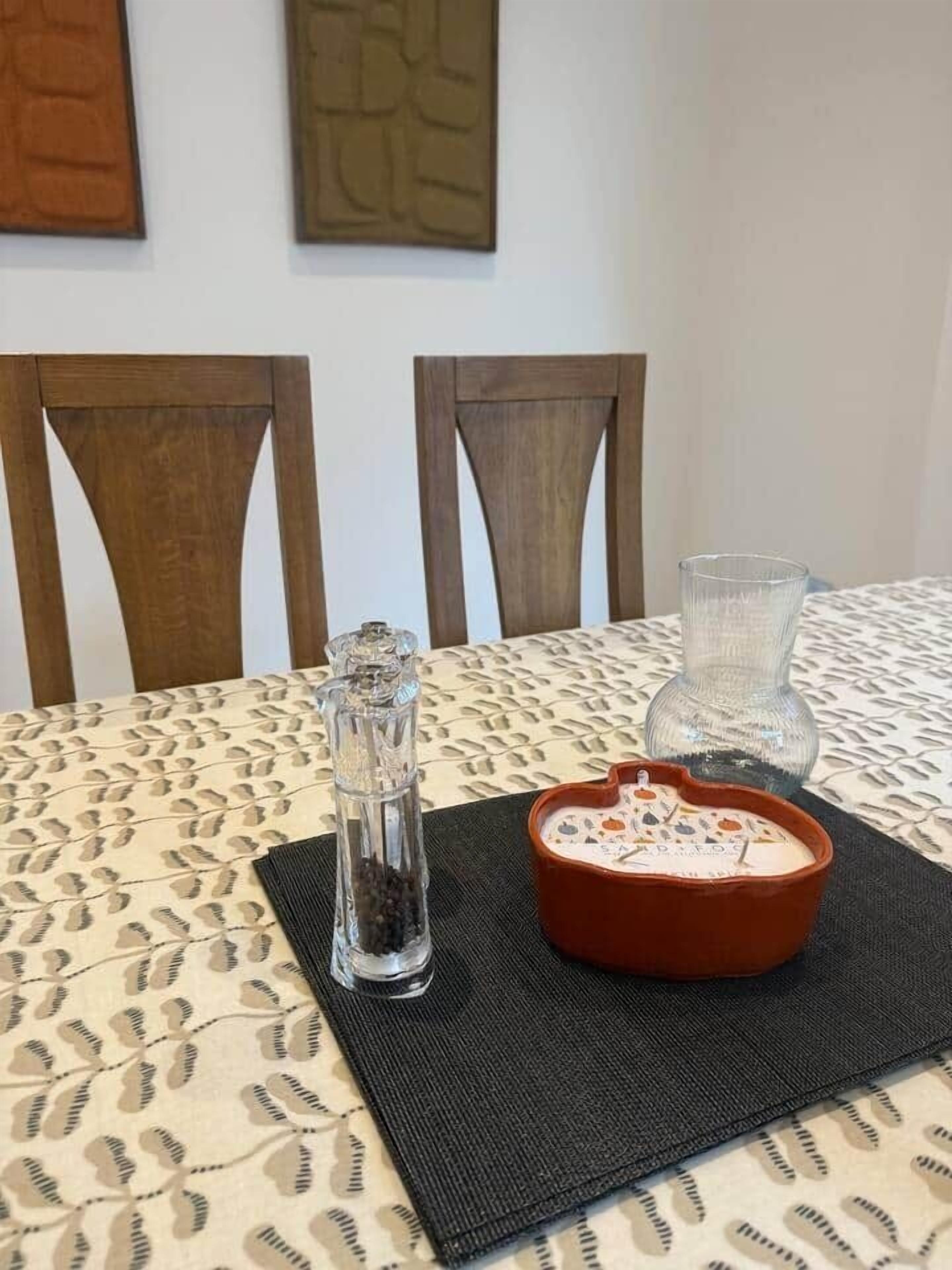 A dining table with a patterned tablecloth, a salt and pepper shaker, a glass, and a ceramic dish with food.