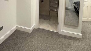 A room with a flat-screen TV mounted on the wall, a door leading to a bathroom, and a large mirror on the right wall.