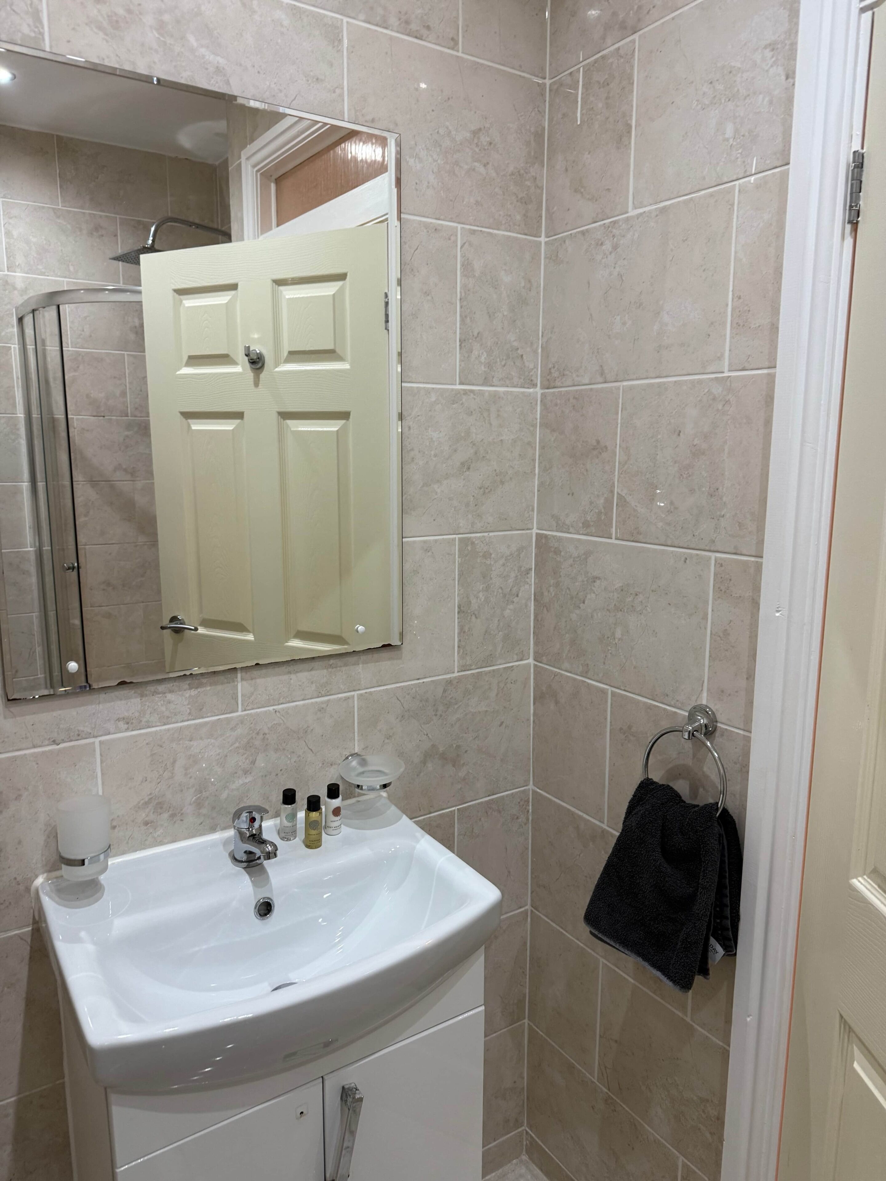 Un baño con lavamanos blanco, espejo y paredes con azulejos.