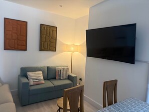 Una sala de estar con un sofá, un televisor montado en la pared y una lámpara.