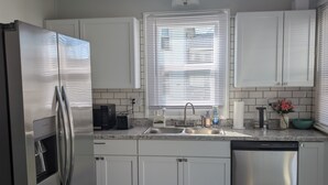 Une cuisine moderne avec des meubles blancs, des appareils en acier inoxydable, un évier double et un tapis à motifs.