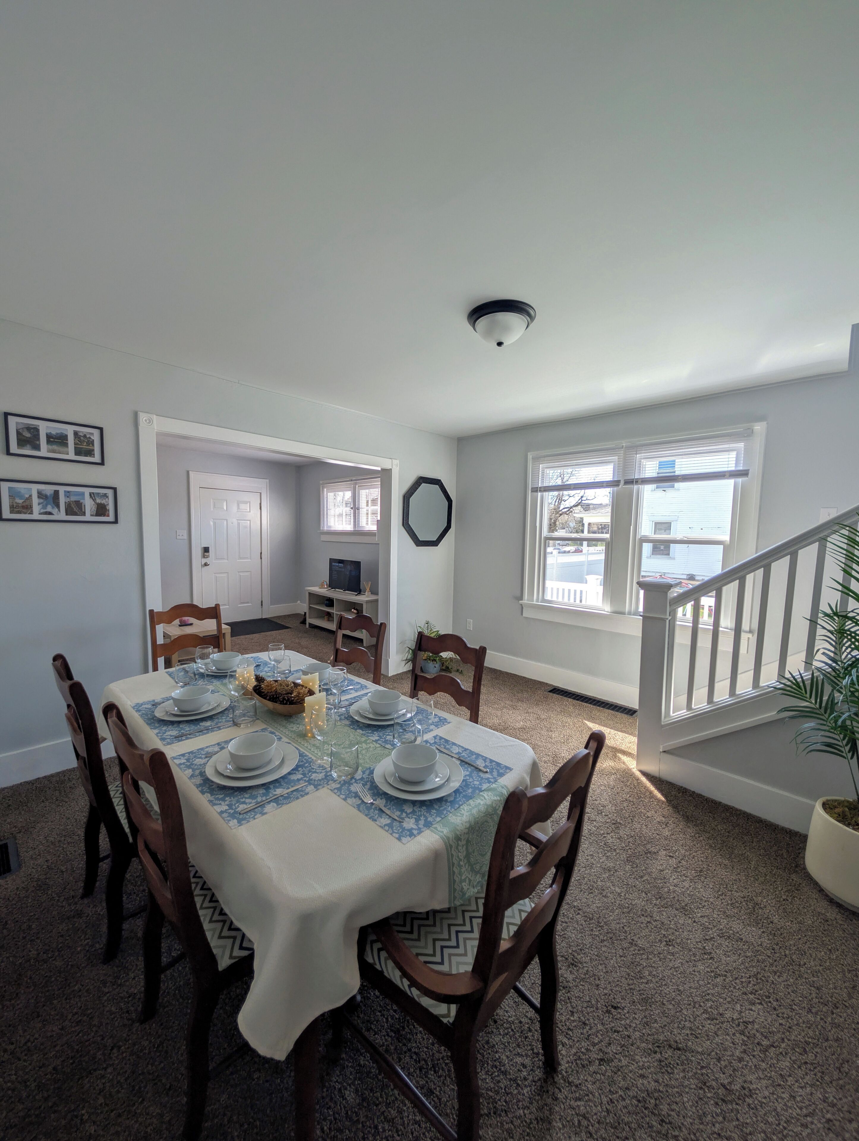A dining area with a table set for four, a white door, a mirror, and a staircase.