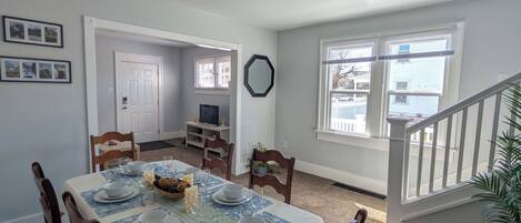 A dining area with a table set for four, a white door, a mirror, and a staircase.