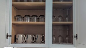 Une cuisine avec un meuble contenant des bocaux en verre, des verres à vin et des tasses.