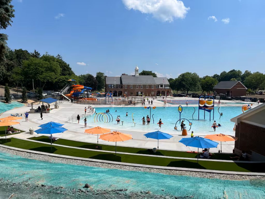 Ein Schwimmbadbereich mit mehreren Bahnen, Sonnenschirmen und einer Wasserrutsche.