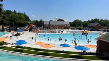 Ein Schwimmbadbereich mit mehreren Bahnen, Sonnenschirmen und einer Wasserrutsche.