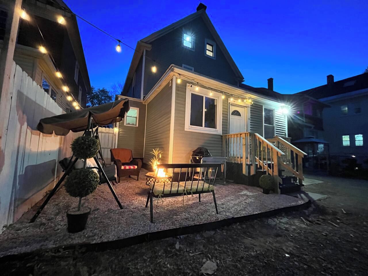 A house with a porch, a small fire pit, and string lights.