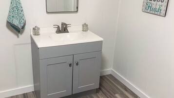 Une salle de bain avec un lavabo blanc, des meubles gris, un miroir, une serviette et un tapis.
