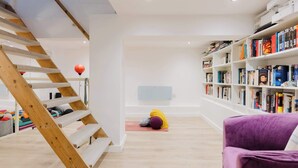 Una habitación con una escalera de madera, un tapete de yoga, una silla morada y una estantería llena de libros.