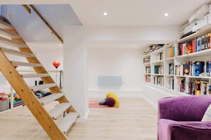 Ein Zimmer mit einer Holztreppe, einer Yogamatte, einem violetten Sessel und einem Bücherregal voller Bücher.