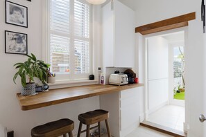 Eine Küche mit einer Holzausziehtischplatte, zwei Barhocker, einem Toaster und einer Topfpflanze.