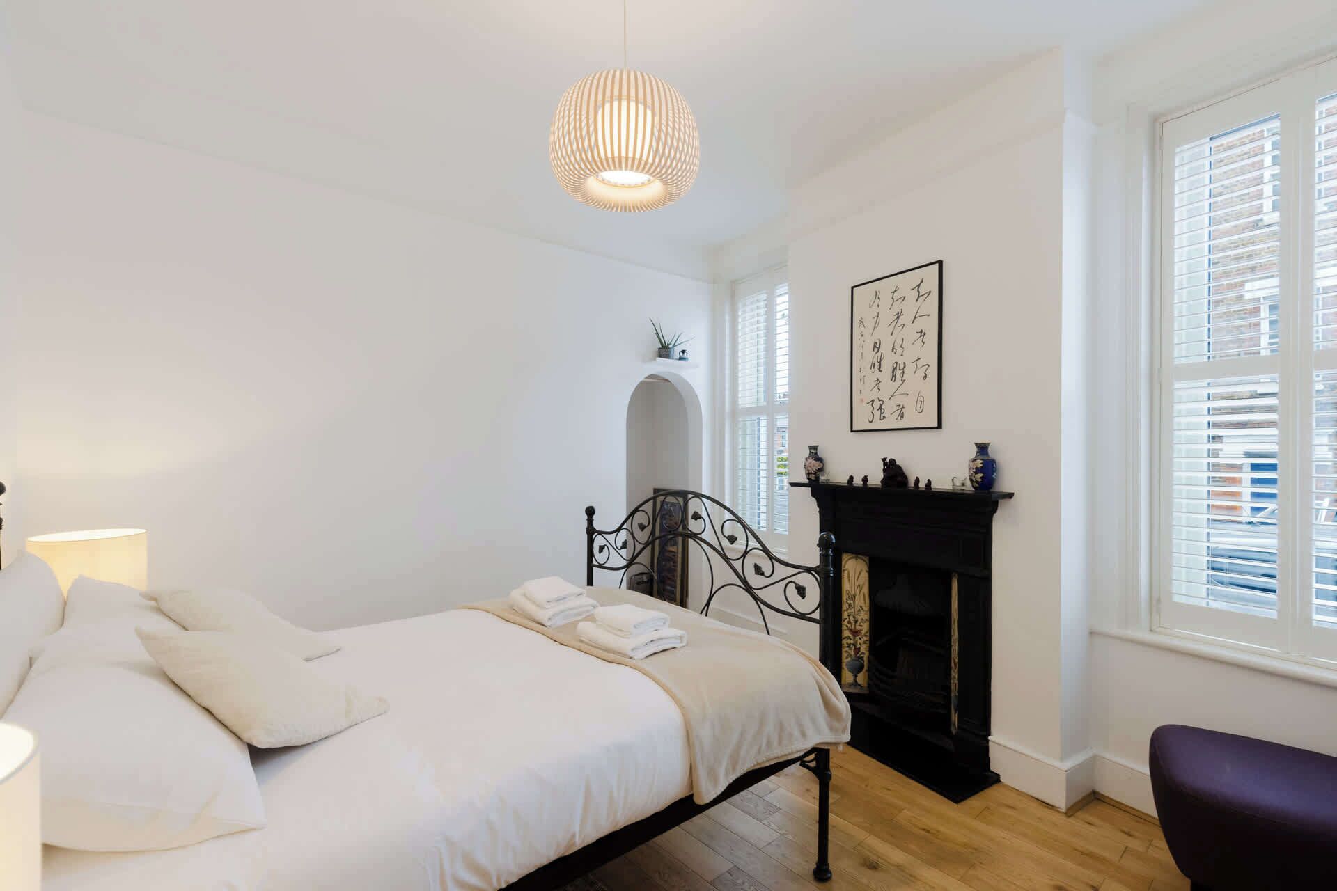 Een slaapkamer met een bed, een open haard, een raam met zonwering en een hanglamp.