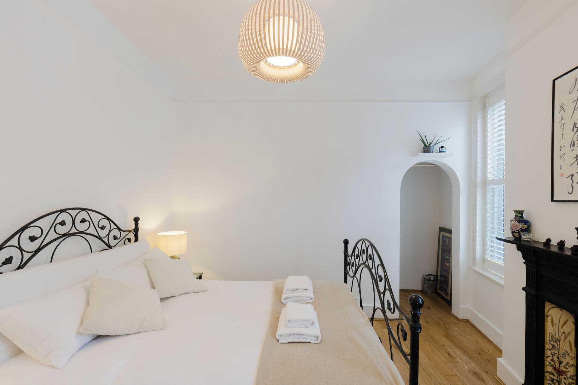 Een slaapkamer met een bed, nachtlampen, een hanglamp, een open haard en een kleine plant op een plank.