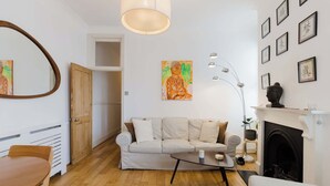Una sala de estar con un sofá, una mesa de centro, una chimenea y obras de arte en las paredes.