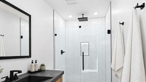 A modern bathroom with a large mirror, a black sink, a toilet, and a shower area.