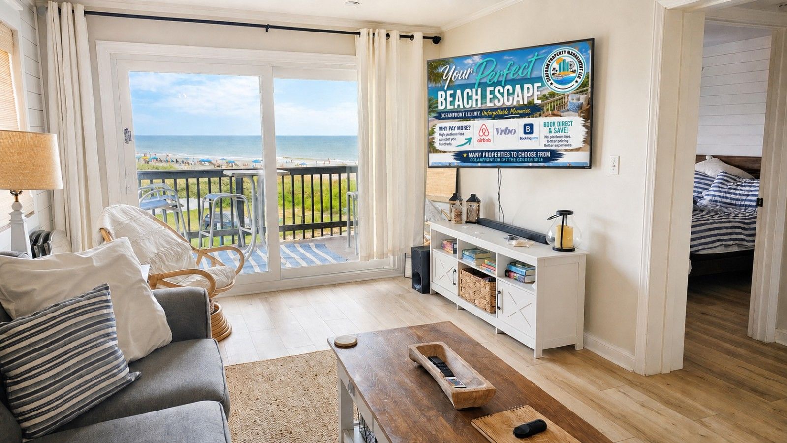 A living room with a view of the beach, a flat-screen TV mounted on the wall, a sofa, a coffee table, and a wooden sideboard with storage.