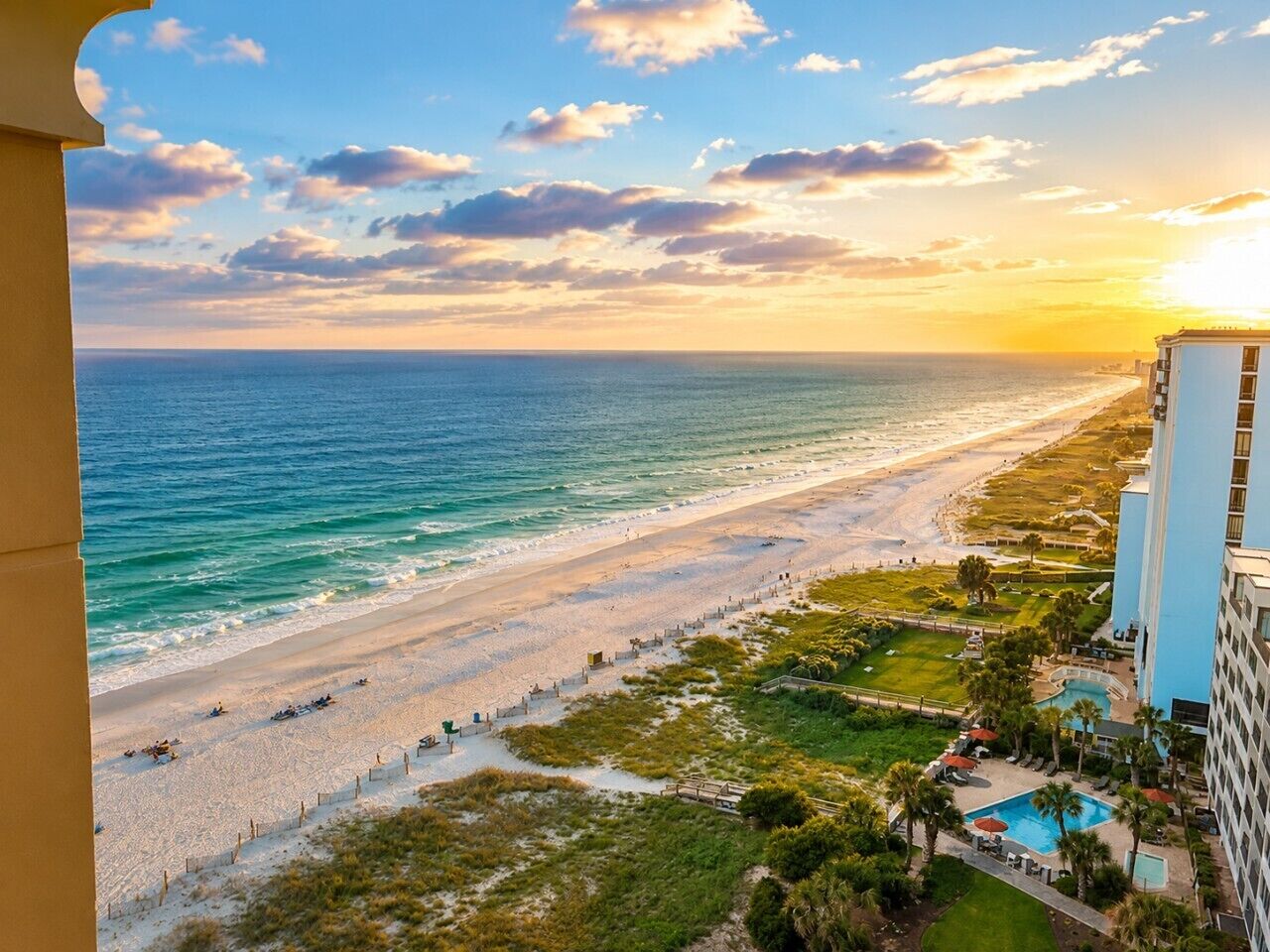 A beach view from a balcony overlooking a sandy beach and ocean, with a hotel building on the right.
