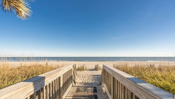 A wooden boardwalk leading to a beach with clear skies.