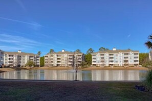 A multi-story hotel with a reflective lake in front, surrounded by greenery. - Lakefront 3br Luxury Condo - MB (Myrtle Beach)