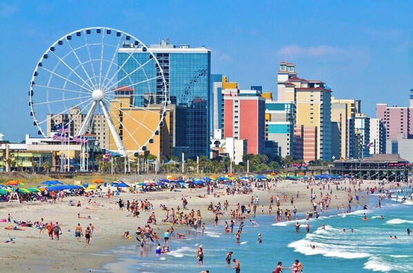 A beach with a Ferris wheel, a crowded beach, and a cityscape with tall buildings. - Lakefront 3br Luxury Condo - MB (Myrtle Beach)