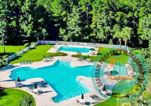 A large swimming pool with a wavy design, surrounded by lounge chairs and a fenced area. - Golfers Dream True Blue Golf Resort Pawleys Island (Pawleys Island)