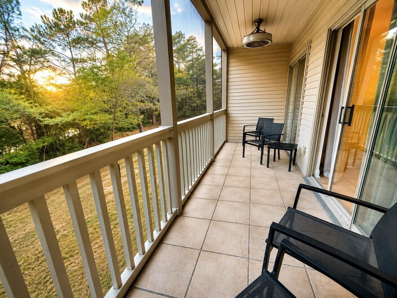 A covered balcony with a railing, two chairs, and a table.