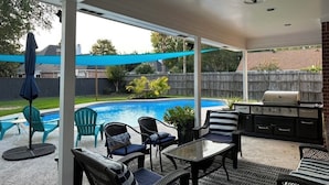 Ein überdachter Patio-Bereich mit Pool, Gartenmöbeln und Grill.