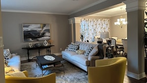 Ein Wohnzimmer mit einer Couch, einem Couchtisch und gelben Stühlen. Es gibt einen Essbereich mit einem Kronleuchter und einem Tisch.