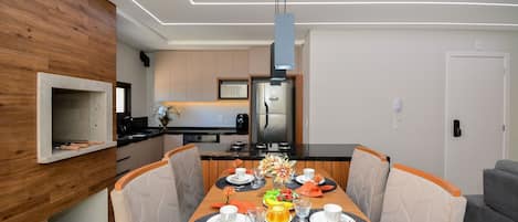 A modern dining area with a wooden table, chairs, and a kitchen in the background.