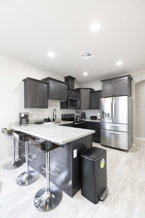 Una cocina moderna con gabinetes oscuros, electrodomésticos de acero inoxidable, una encimera de granito y una isla central con taburetes de bar.