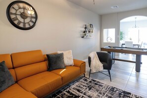 Una sala moderna con un sofá, una silla, un reloj, estanterías y vistas a otra habitación.