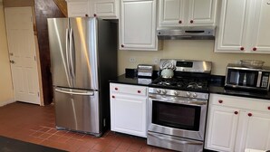 A kitchen with white cabinets, stainless steel appliances, a black countertop, and a tiled floor. - Limbe Guest House in Latham NY (Latham)