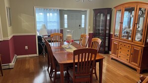 A dining room with a wooden table, chairs, a chandelier, and a china cabinet. - Limbe Guest House in Latham NY (Latham)