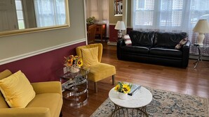A living room with a yellow armchair, a black sofa, a round coffee table, and a mirror on the wall. - Limbe Guest House in Latham NY (Latham)