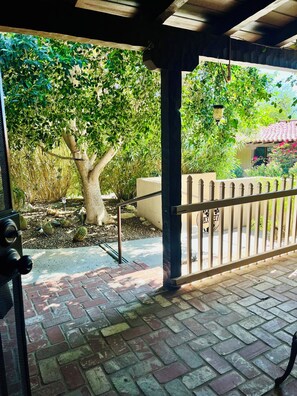 Ein überdachter Patio-Bereich mit Backsteinboden, Metallgeländer und einem Baum im Hintergrund.
