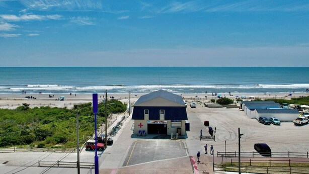 Un edificio frente a la playa con estacionamiento, una playa al fondo y cielo despejado.
