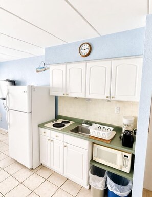 A compact kitchen with white cabinets, a stove, a sink, a microwave, and a clock on the wall.